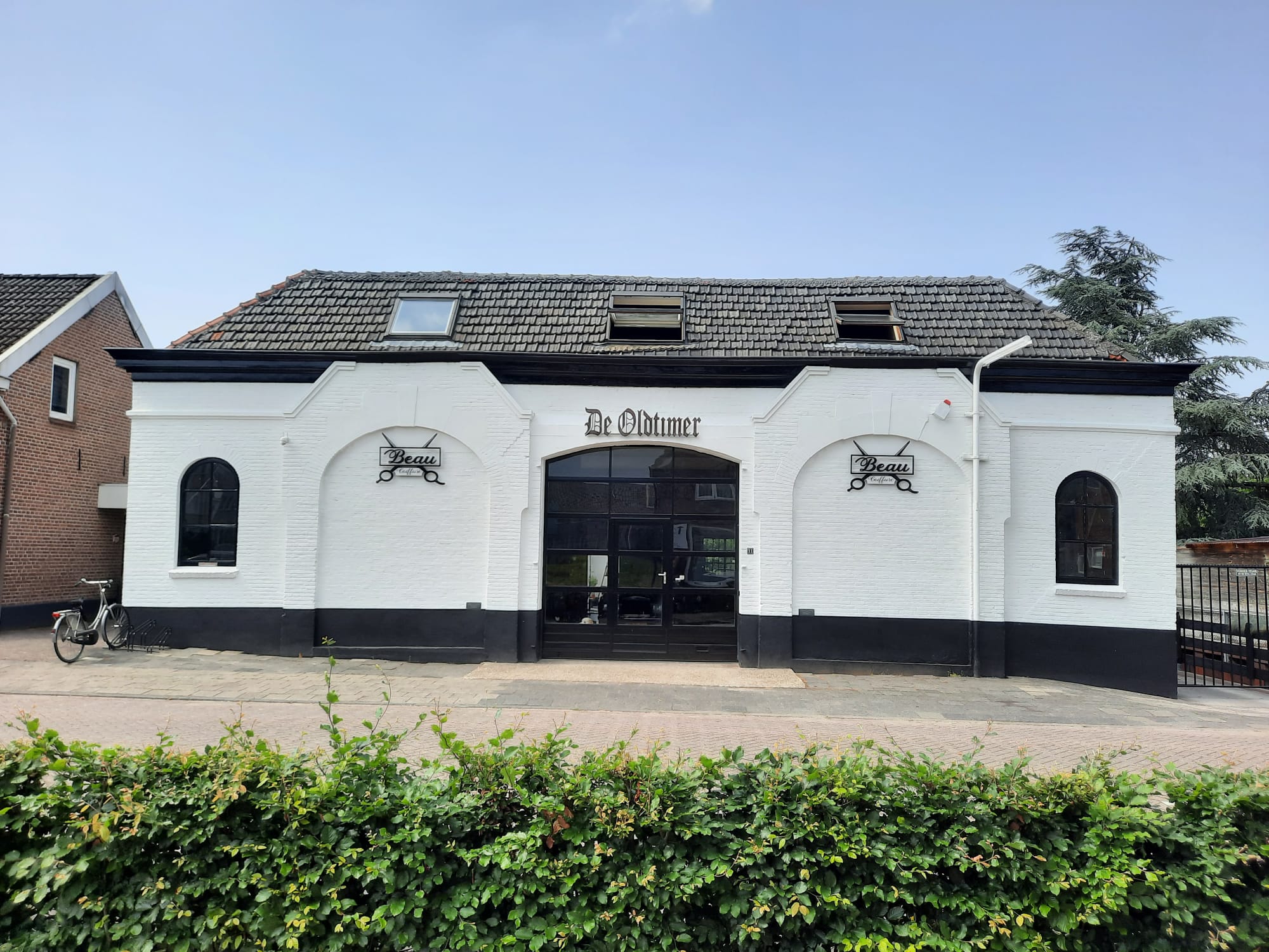De witte buitengevel van Beau Coiffure met zwarte plint en boogramen
